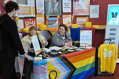 A conference stall with Progress flag and LGBT+ Lib Dem resources