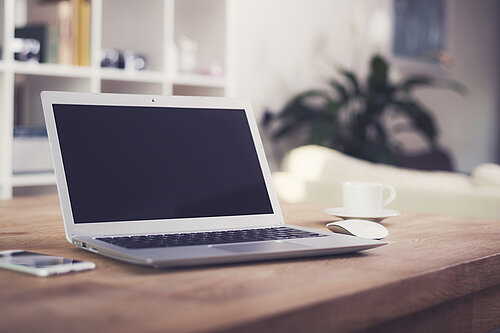 A laptop, phone and coffee cup on a table.