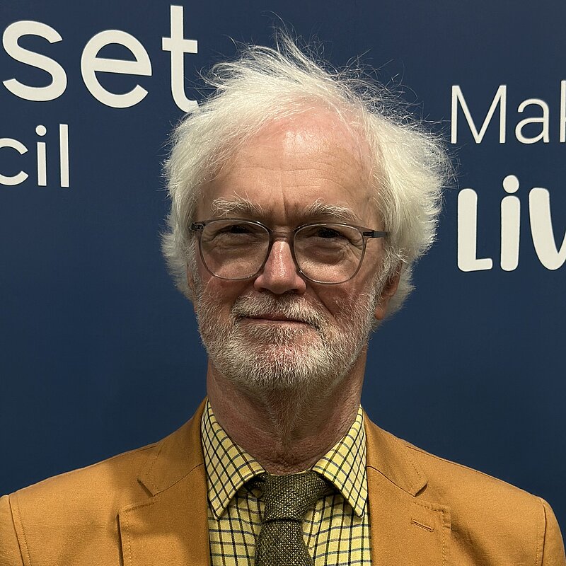 Dorset Councillor for Sherborne Rural ward and Sherborne Town Council Councillor, Robin Legg stood in front of a Dorset Council graphic at the Dorset Council Count on the 3rd May 2024