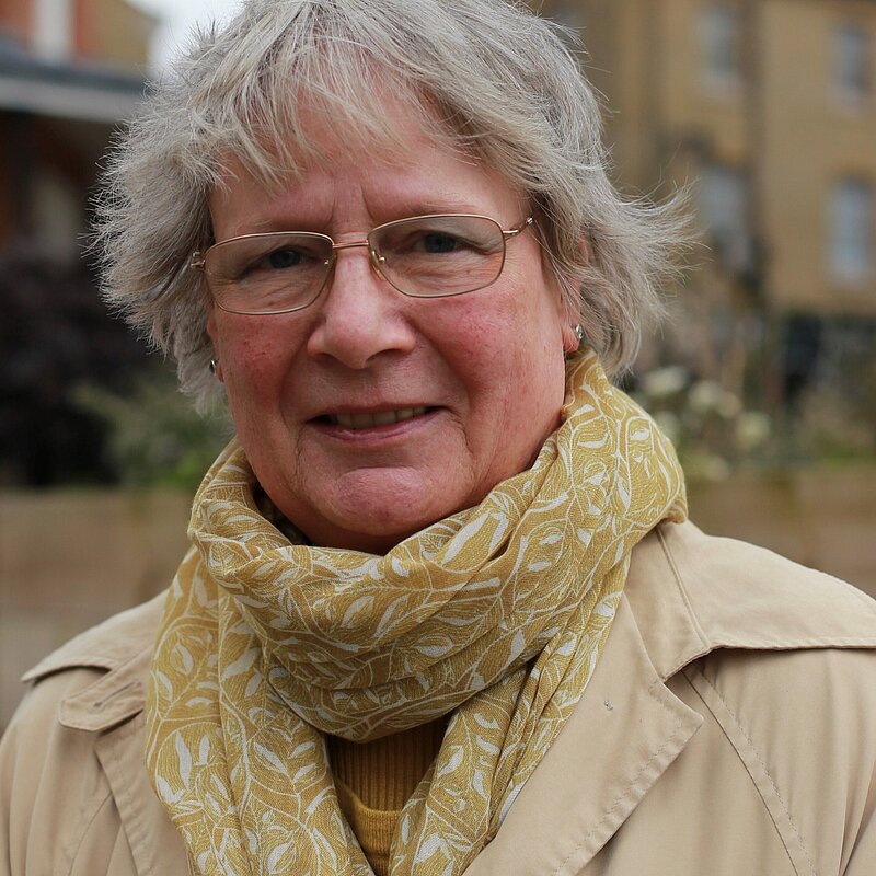 Frances Hogwood in 2019, wearing a beige trench coat and yellow scarf