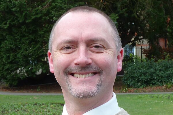 David Taylor wearing a tan sweater and a yellow tie.