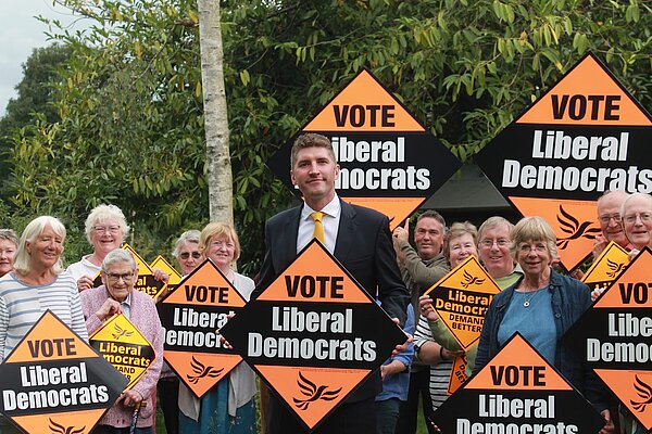 A group of activists with Edward Morello standing in the middle, all are holding Lib Dem orange placards 