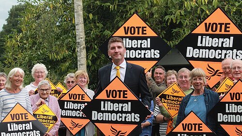 A group of activists with Edward Morello standing in the middle, all are holding Lib Dem orange placards 