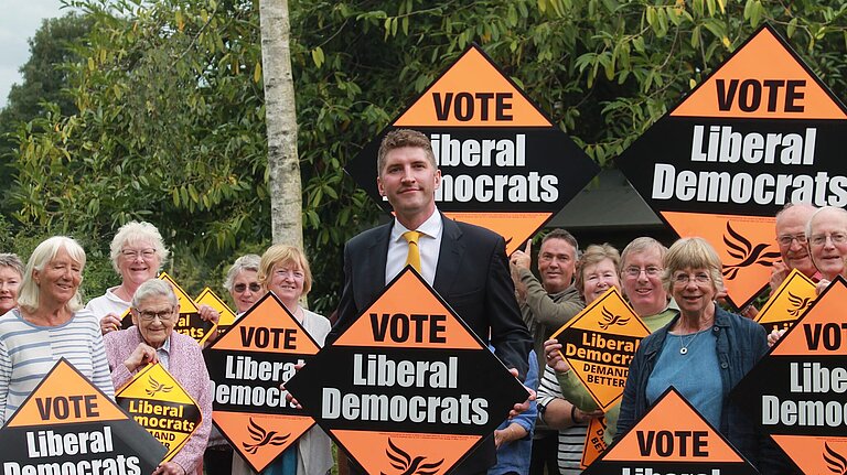 A group of activists with Edward Morello standing in the middle, all are holding Lib Dem orange placards 