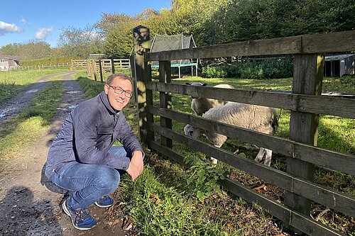 Tom Gordon in a field crouched next to a sheep in a pen