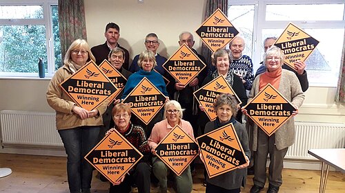 A group of Lib Dem activists holding placards in a Village hall with Edward Morello