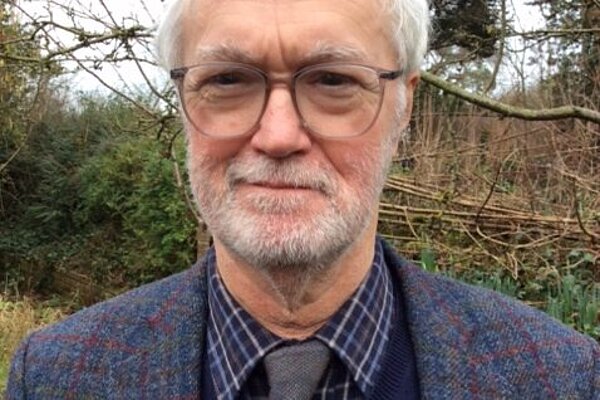 Robin Legg with glasses and sweater standing in front of tree.