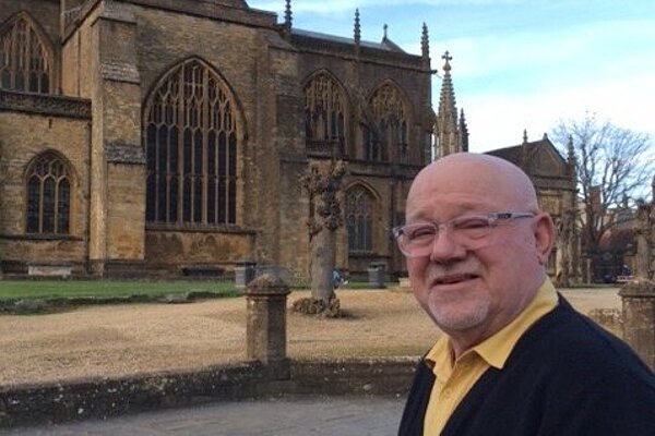 Jon Andrews wearing a yellow shirt and black jumper outside of Sherborne Abbey