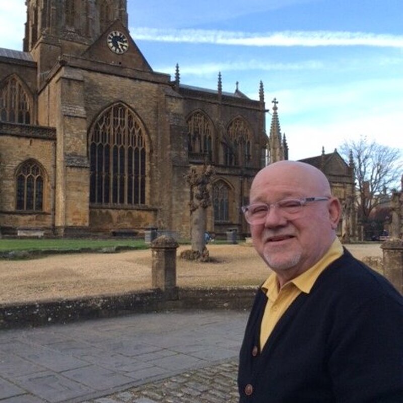 Jon Andrews wearing a yellow shirt and black jumper outside of Sherborne Abbey