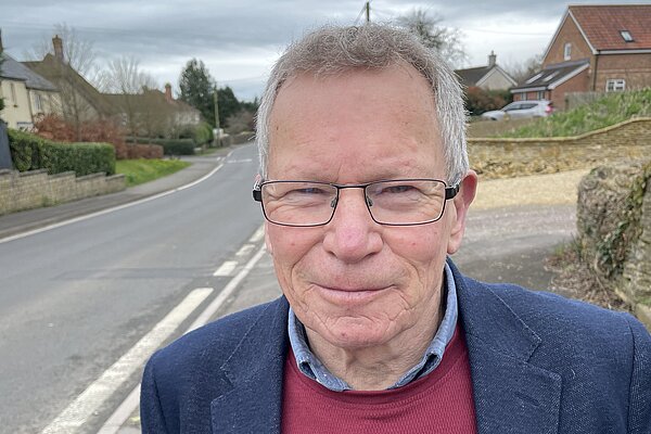 Chris Kippax wearing ared jumper and navy blue suit jacket in Longburton