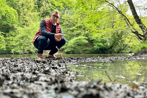 Tom Gordon crouching on a bed of stones next to the River Nidd