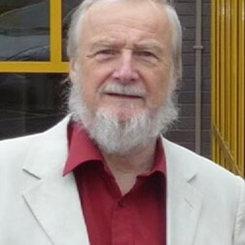 Dave Rickard is an older man with white hair and beard. In this image he is wearing a red shirt and white suit jacket