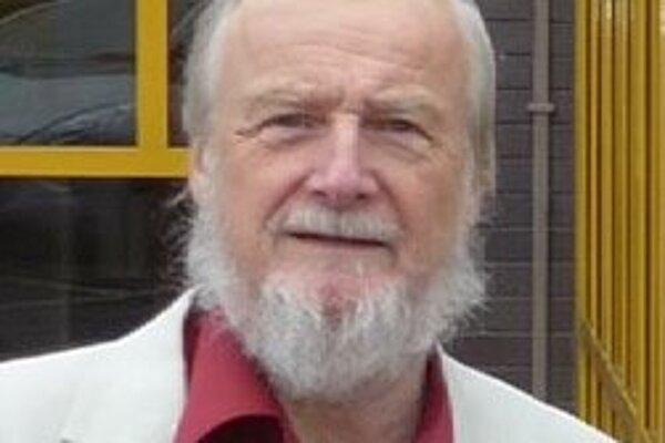 Dave Rickard is an older man with white hair and beard. In this image he is wearing a red shirt and white suit jacket