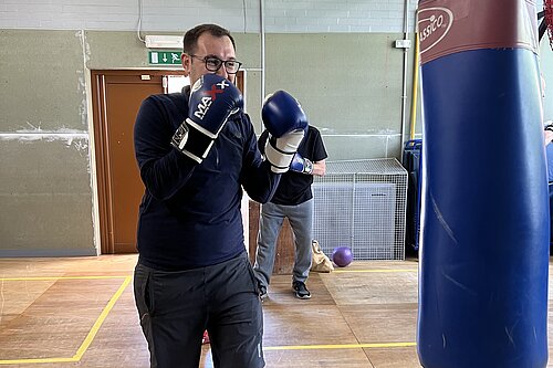 Tom Gordon at a boxing gym with arms up, boxing gloves on and looking at a punchbag