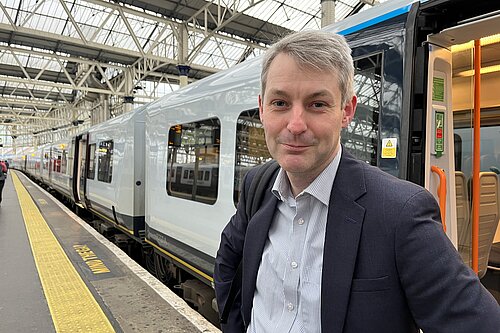 Will Forster at Waterloo station with a train behind him